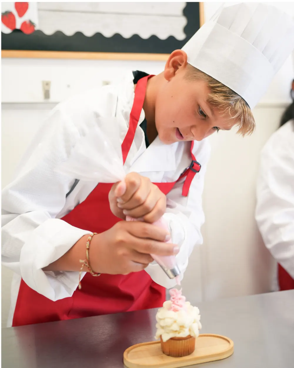 Boy in a chef hat piping icing onto a cupcake at a Master Chef party