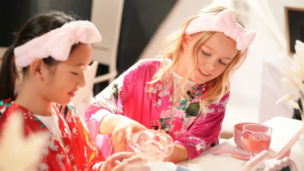 Girls in robes and headbands mixing body mist at the spa table