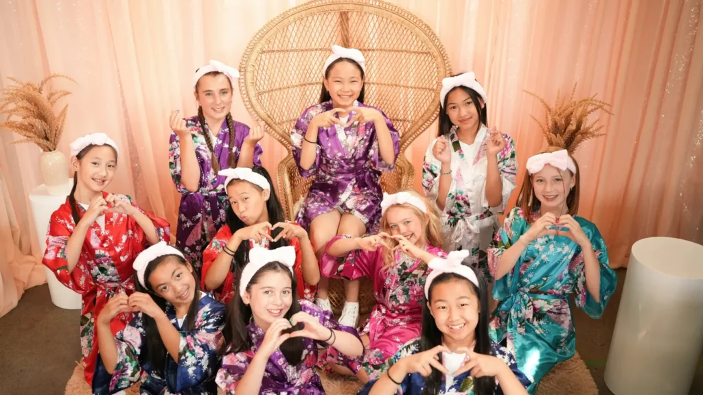 Group of girls in robes making heart hands around the rattan peacock chair