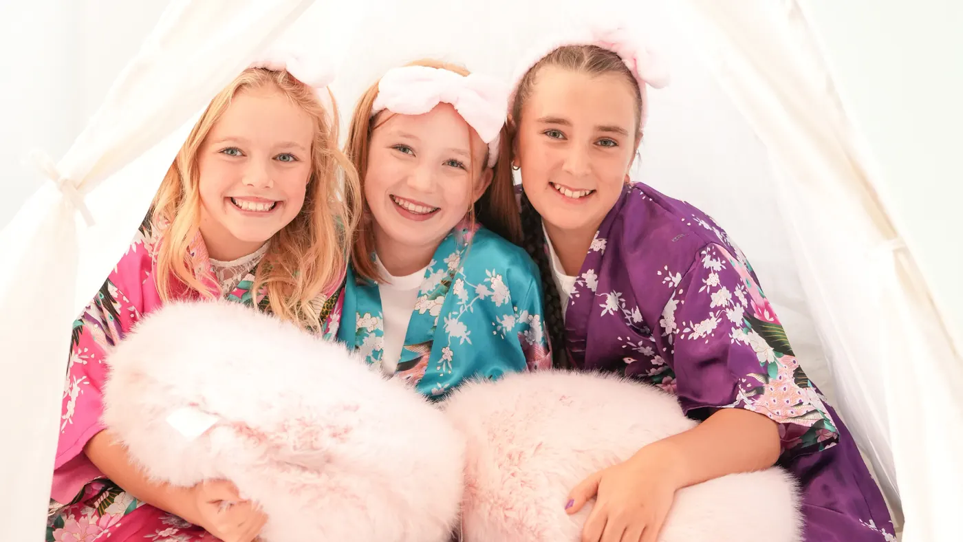 Three friends in satin robes posing in a cozy tent at a spa birthday party