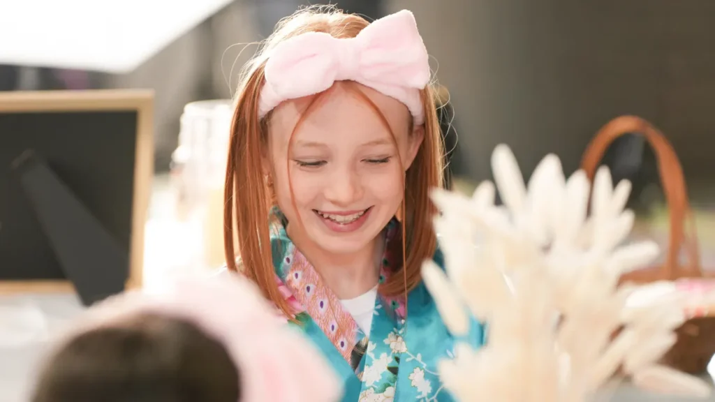 Girl in a satin robe and bow headband smiling at a Glam & Glow spa party