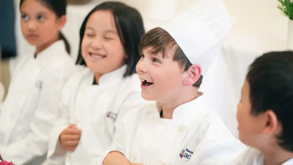 Kids in chef coats laughing together at a Master Chef cooking party