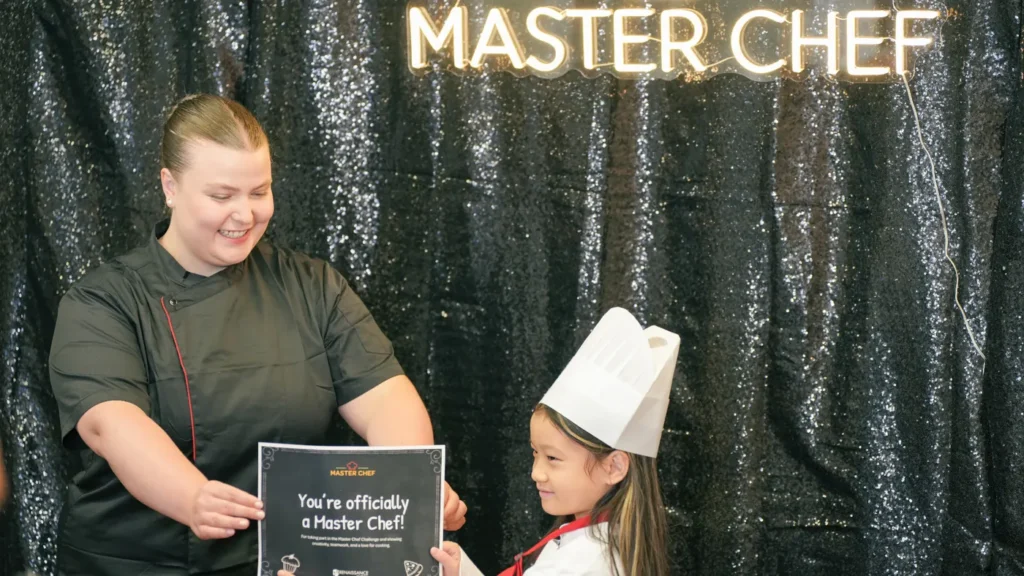 Party host presenting a Master Chef certificate to a child in a chef hat