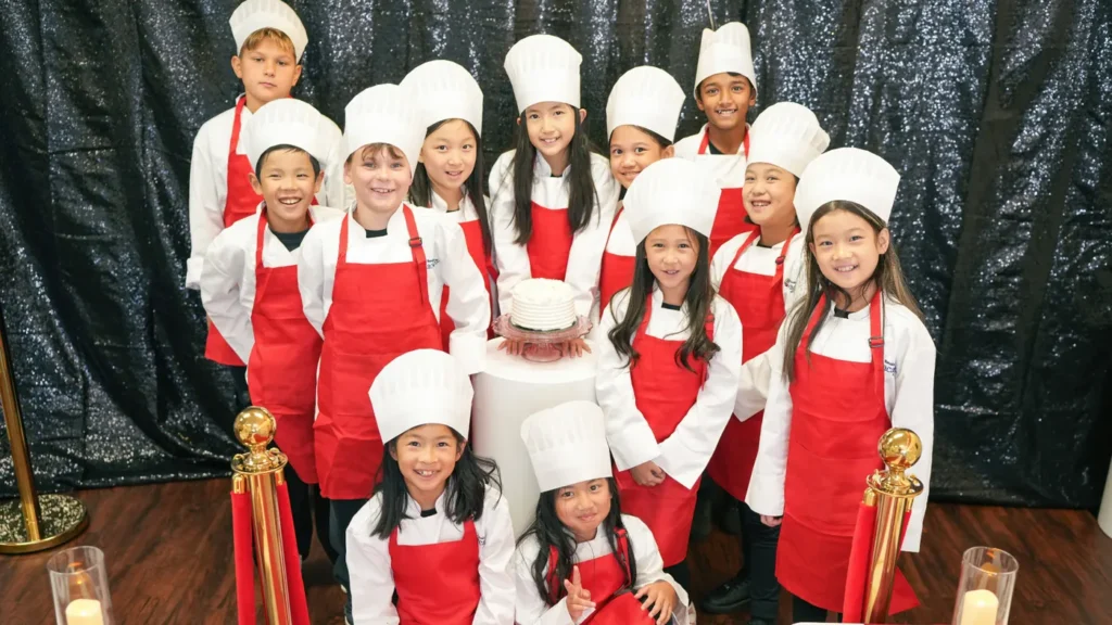 Group of young chefs in hats and red aprons in front of the Master Chef backdrop